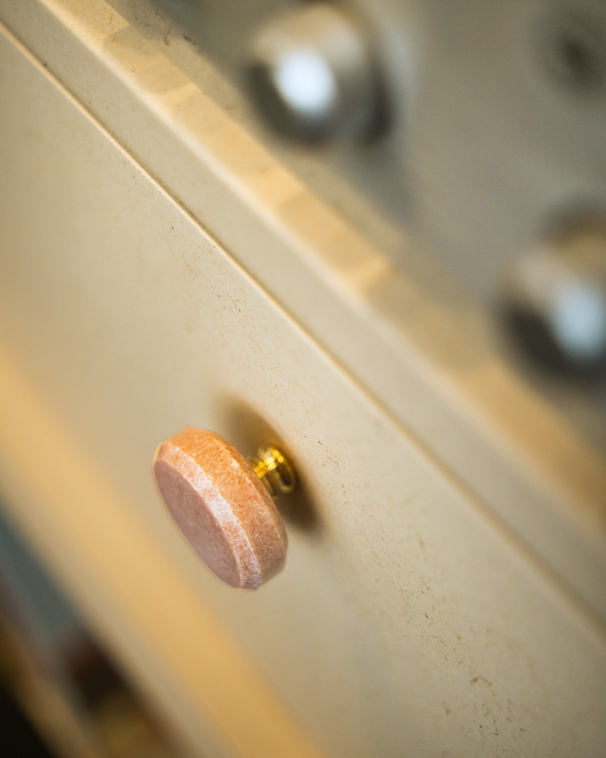 Close detail of the White Pearl finish, fine wood-fibre flecks in the matt surface around a stone and brass knob — Groovaly